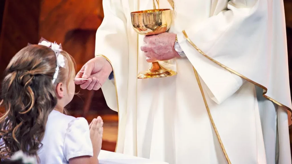 Niña en su primera comunión recibiendo eucaristia - De Bautizos y Familia Cristiana