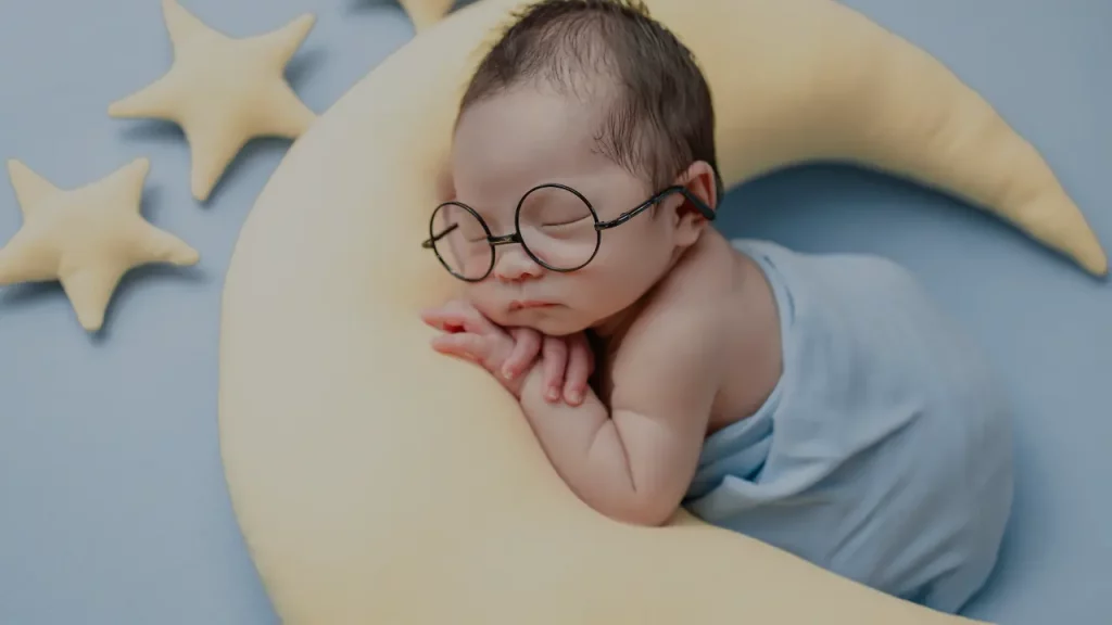 nombre santos para niños, bebé durmiendo con lentes en mueble de luna y estrellas 